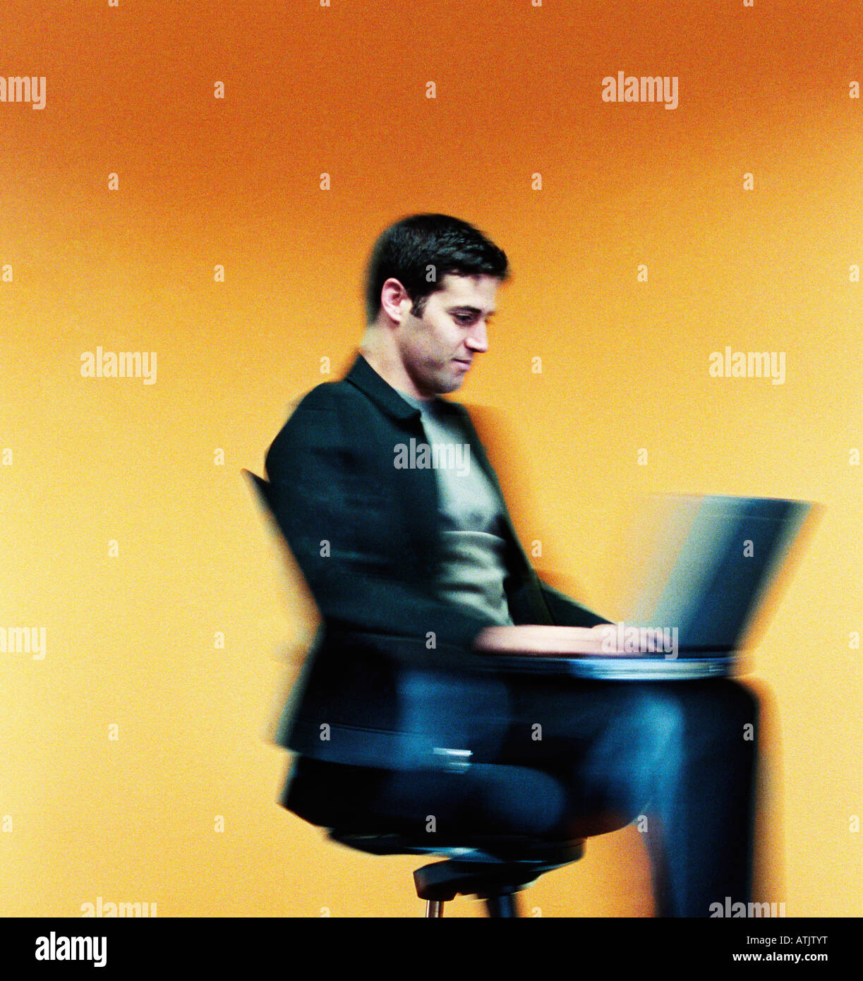 Young adult businessman rolling by on an office chair while typing on his laptop Stock Photo