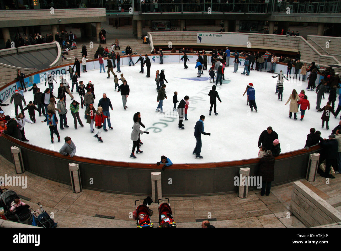 Many people ice skate on a temporary, circular ice rink in an urban