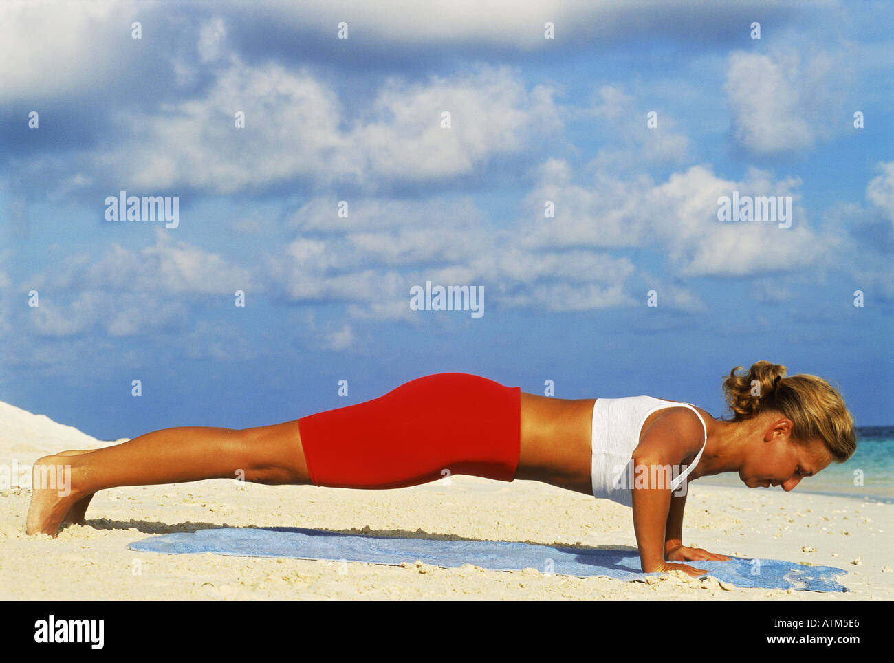 Woman exercising doing push-ups on sandy shore at dawn Stock Photo