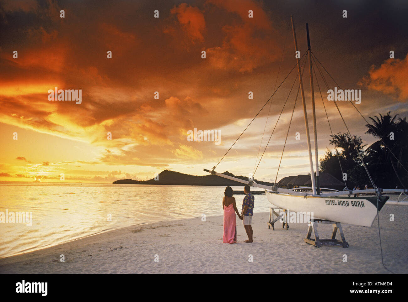 Couple standing on sandy Bora Bora shore holding hands under dramatic sunset sky Stock Photo