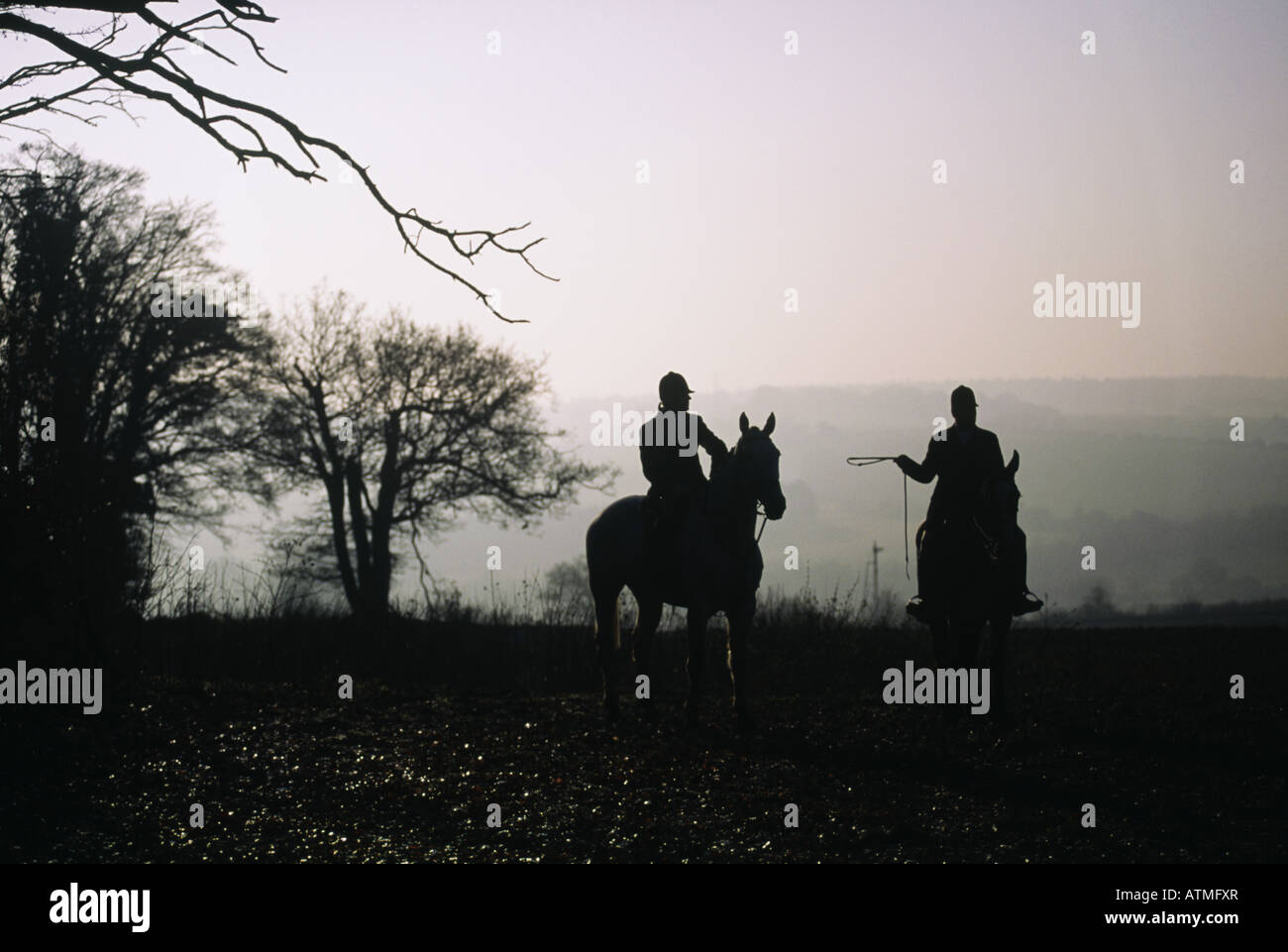 Drag hunting fox hunting Silhouette of two people riders on horseback Against pink sky sunset dawn Stock Photo