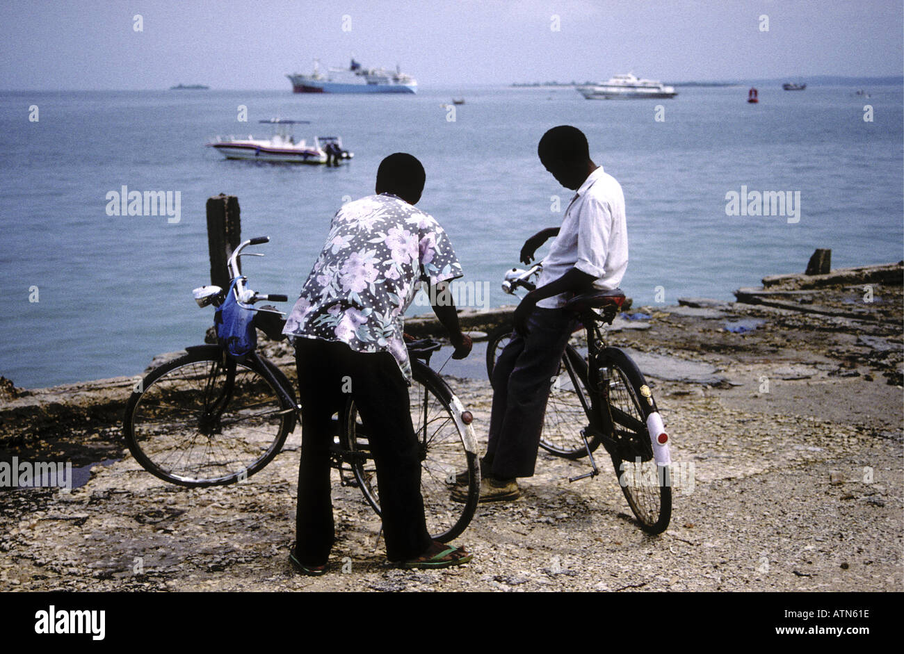 Two young black African men leaning on their bicycles on the waterfront of Zanzibar Tanzania East Africa Stock Photo