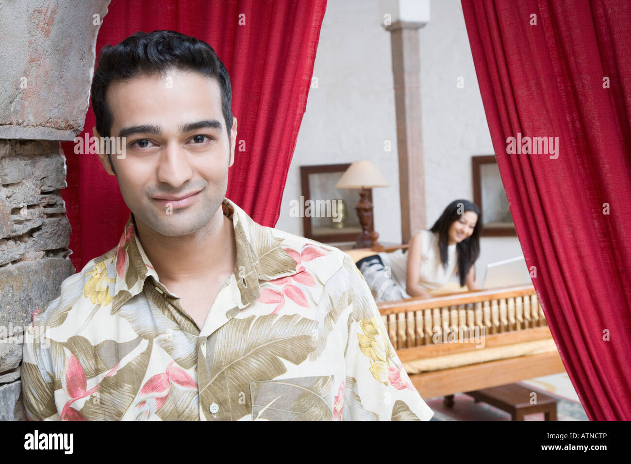 Portrait of a young man smiling with a young woman lying on the bed in ...