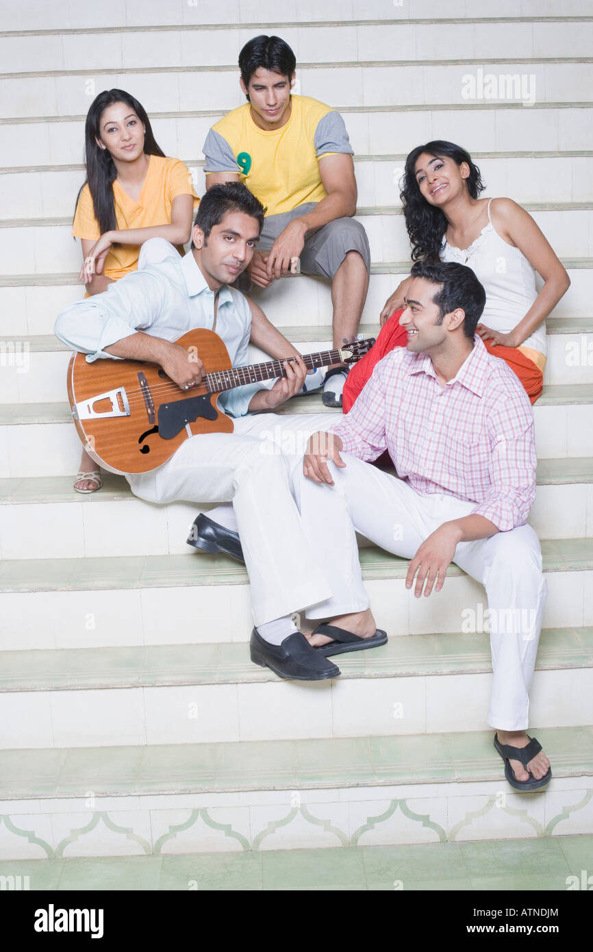 Young man playing a guitar with his friends sitting with him Stock Photo