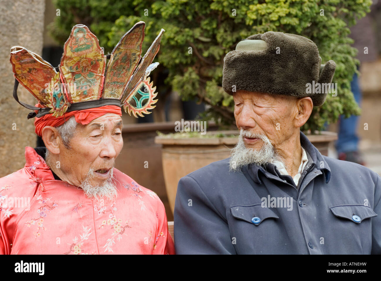 Naxi Dongba Shaman Priest And Old Distinguished Gentleman Sitting On Bench, Lijiang, Old City, Sifang Square, Yunnan, China Stock Photo