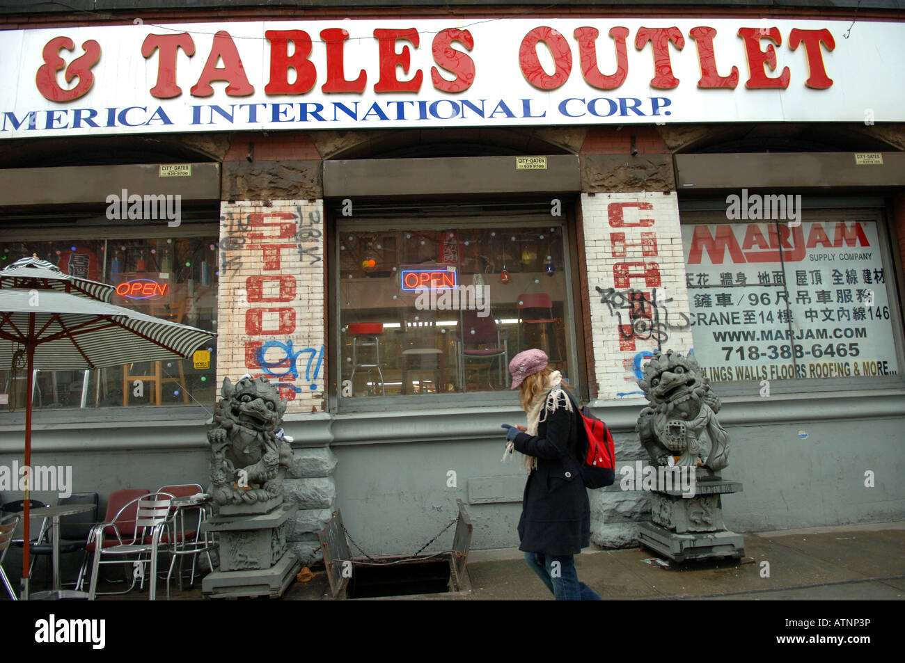 Trendy woman walks past grungy restaurant supply seller on the changing Bowery in NYC Stock Photo
