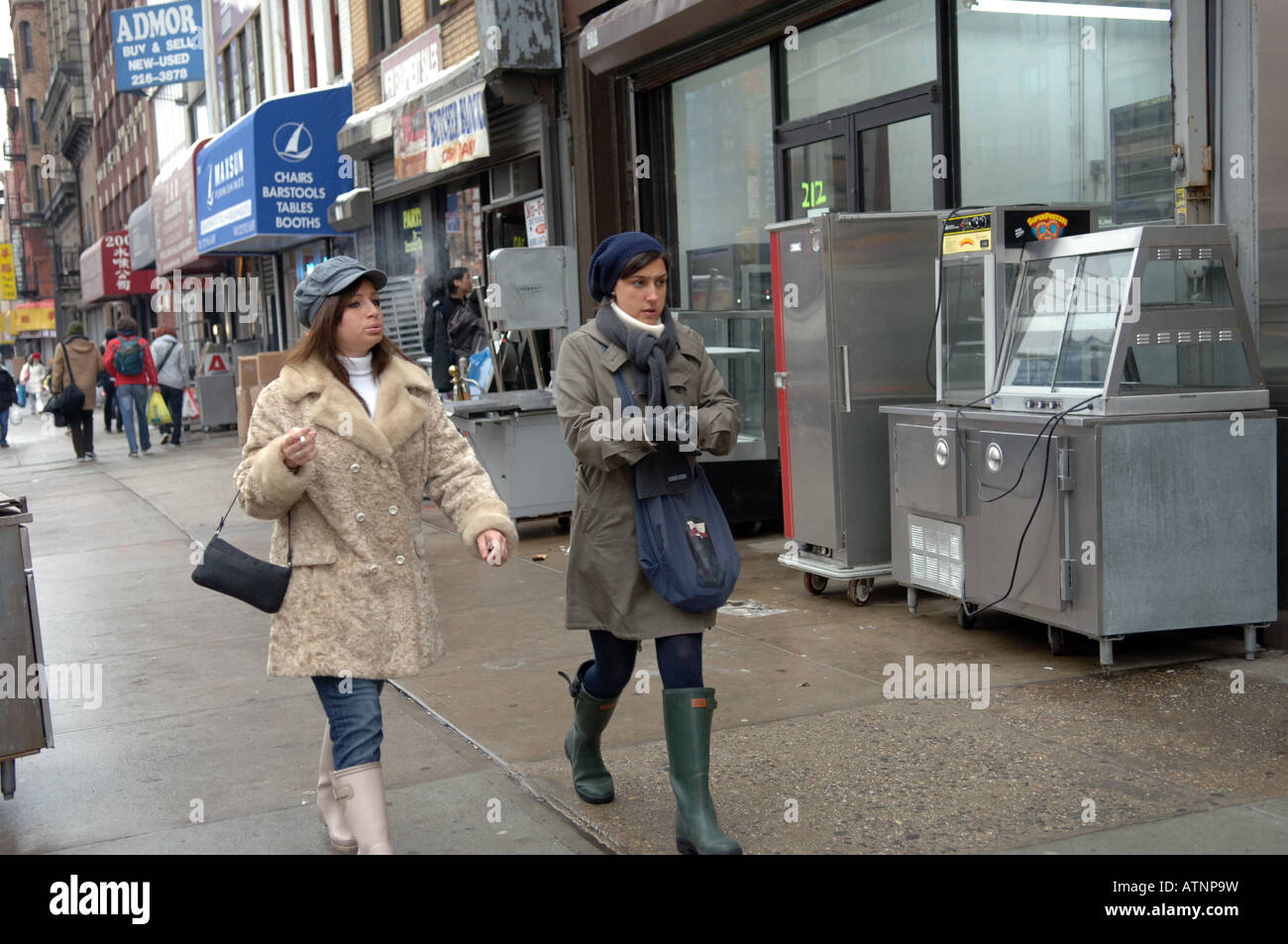 Trendy women walk past grungy restaurant supply sellers on the changing Bowery in NYC Stock Photo