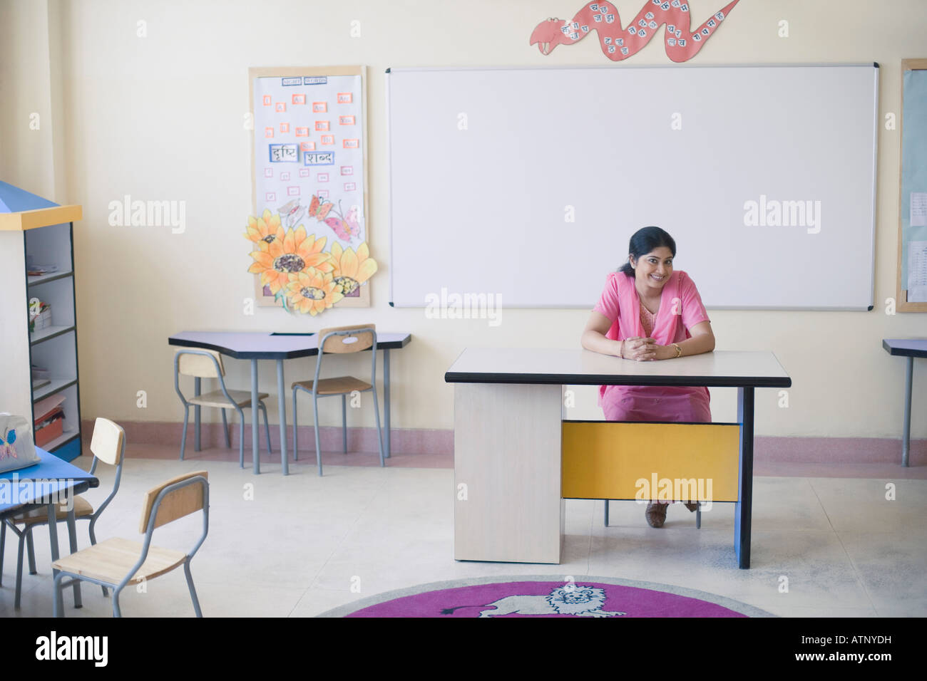 Portrait of a mid adult woman sitting at a desk and smiling in a classroom Stock Photo