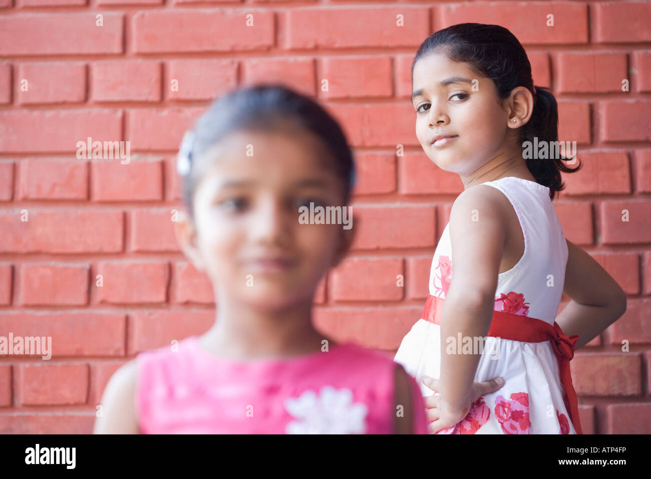 Portrait of two schoolgirls standing in front of a brick wall and smiling Stock Photo