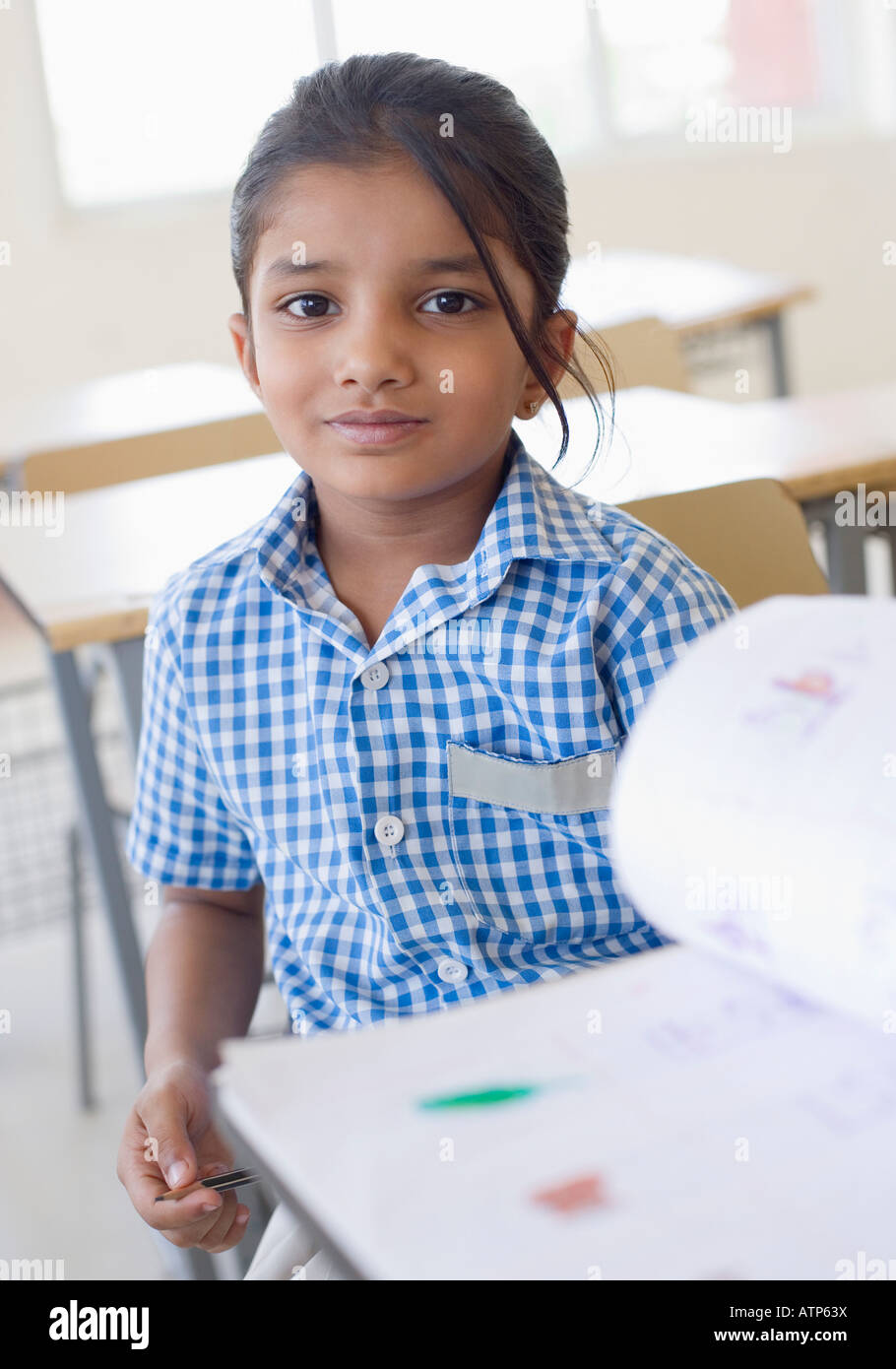 Portrait of a schoolgirl sitting at a desk with a book in front of her ...