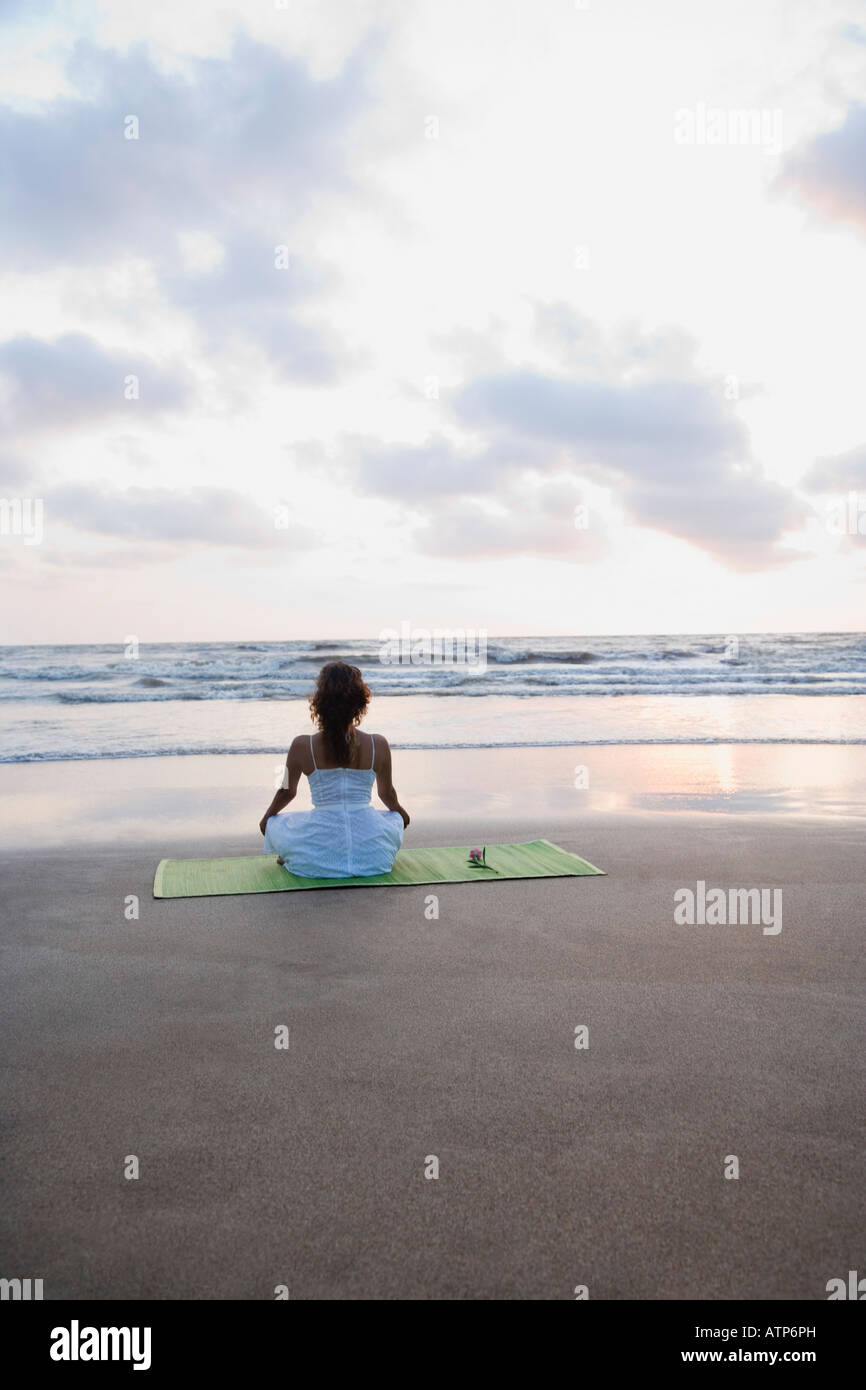 Rear view of a young woman meditating on the beach Stock Photo - Alamy