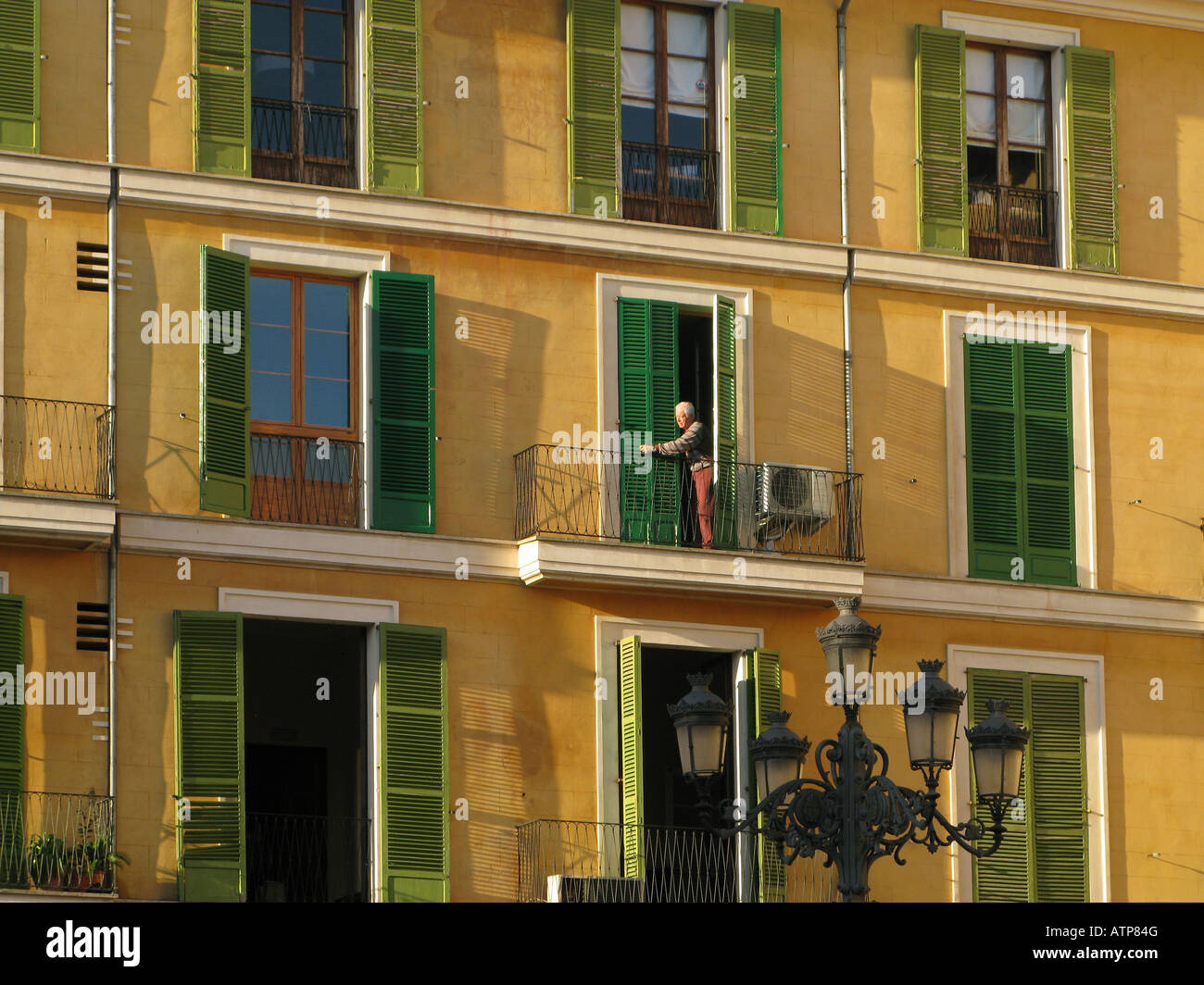 A man on one of the balconies on Plaza Major, Palma, Mallorca. An ornate street lamp is in the foreground Stock Photo