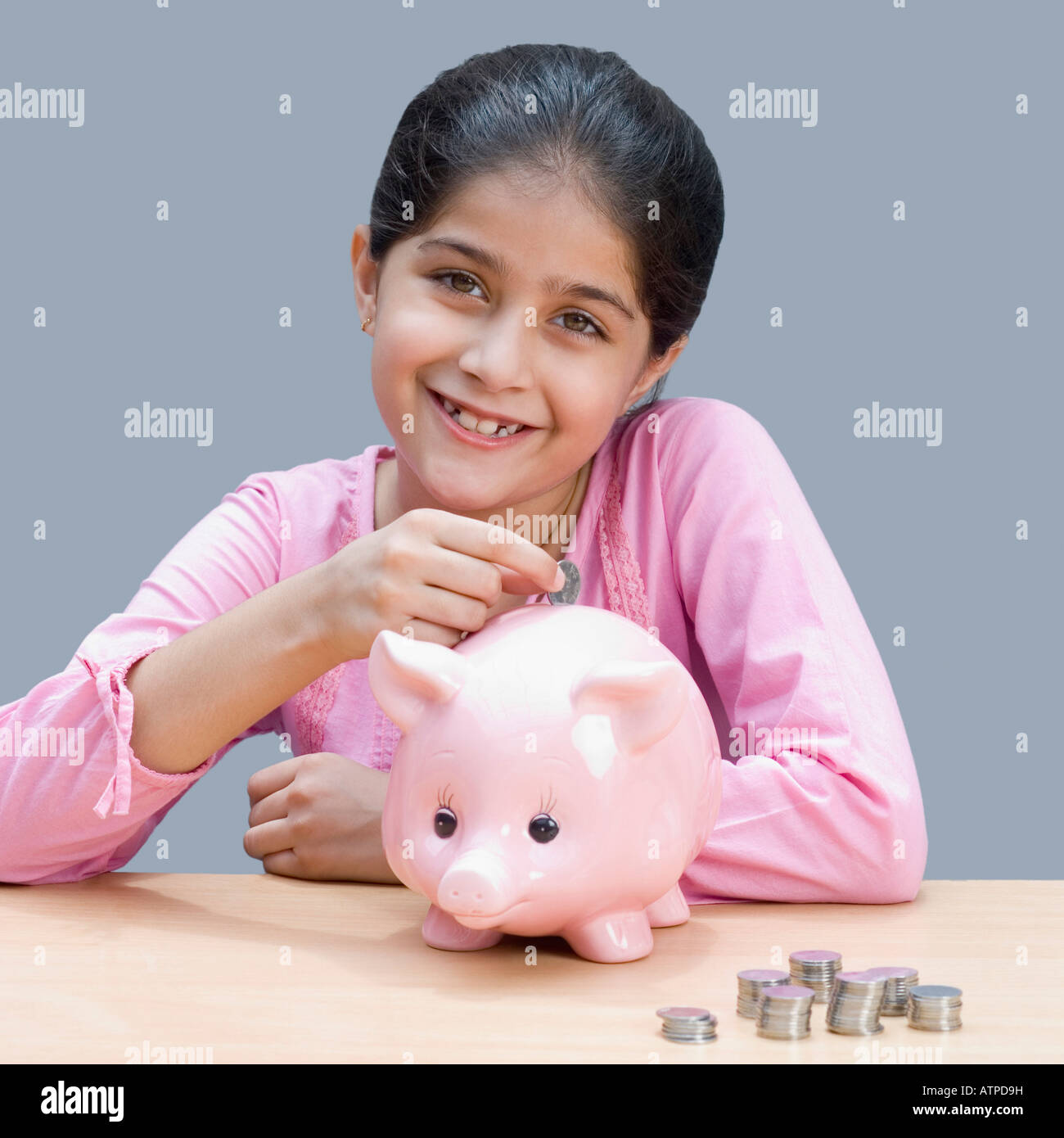 Portrait of a girl putting a coin into a piggy bank and smiling Stock ...