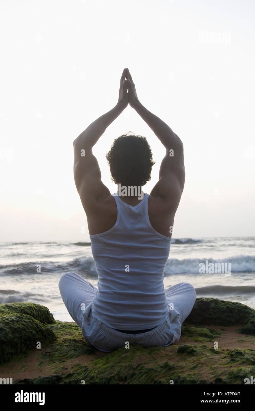 Rear view of a young man meditating on the beach Stock Photo