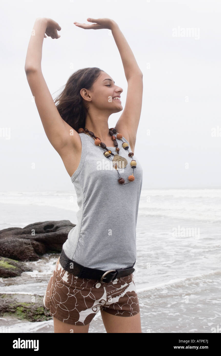 Young woman standing on the beach with her arms raised and smiling ...