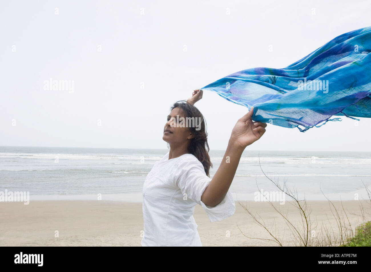 Side profile of a young woman running with her shawl on the beach Stock Photo