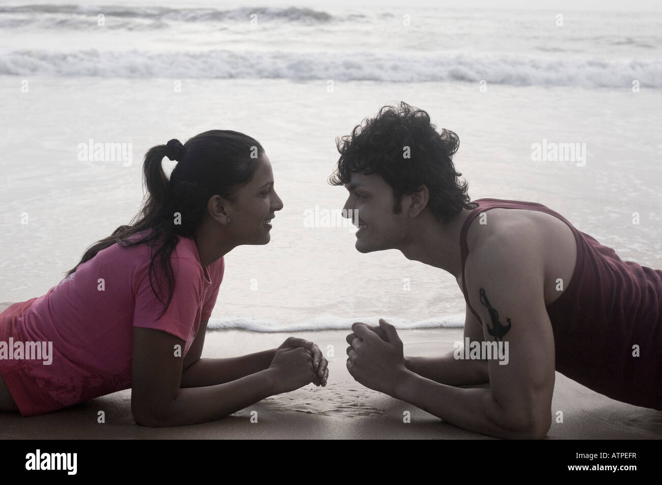 Side profile of a young couple lying on the beach and looking at each ...
