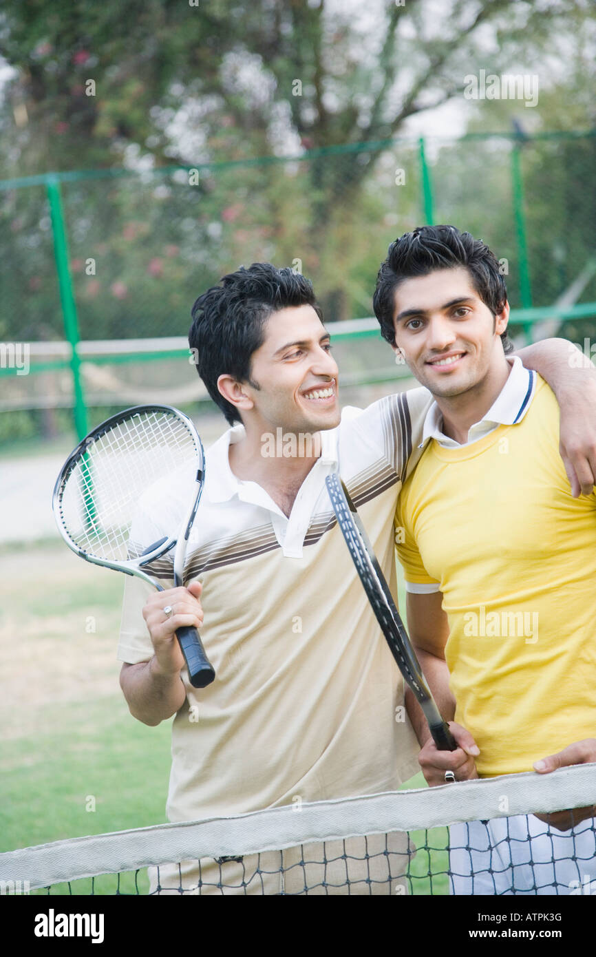 Two young men holding tennis rackets in a court and smiling Stock Photo ...
