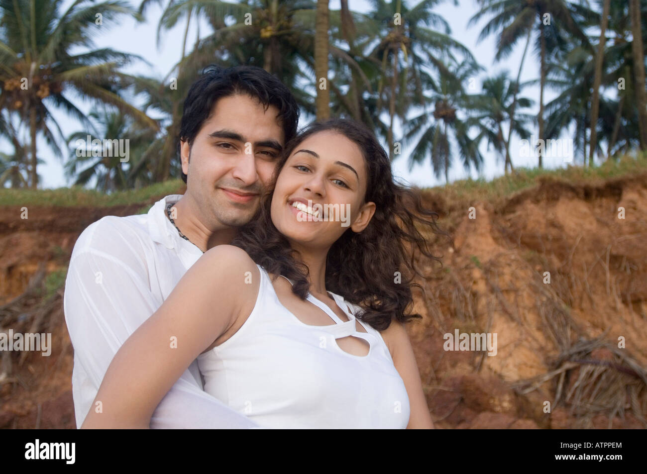 Portrait of a young man embracing a young woman from behind and smiling ...