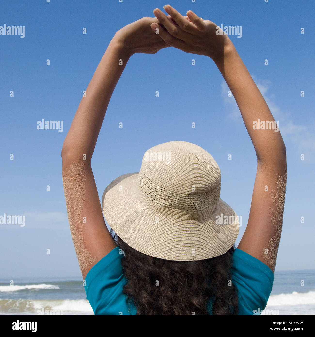 Rear view of a young woman standing with her arms raised on the beach ...