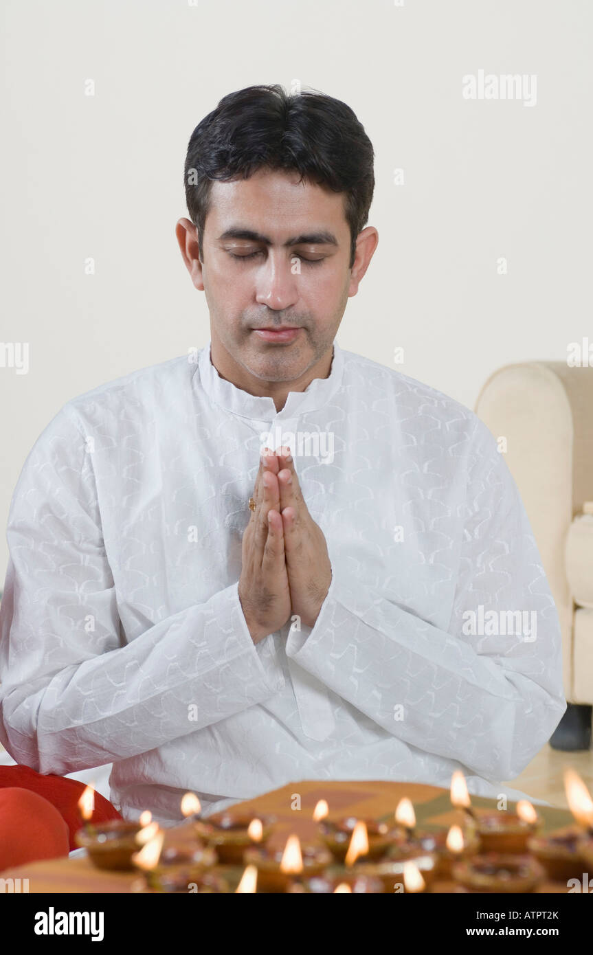 Close-up of a mid adult man praying with oil lamps in front of him Stock Photo