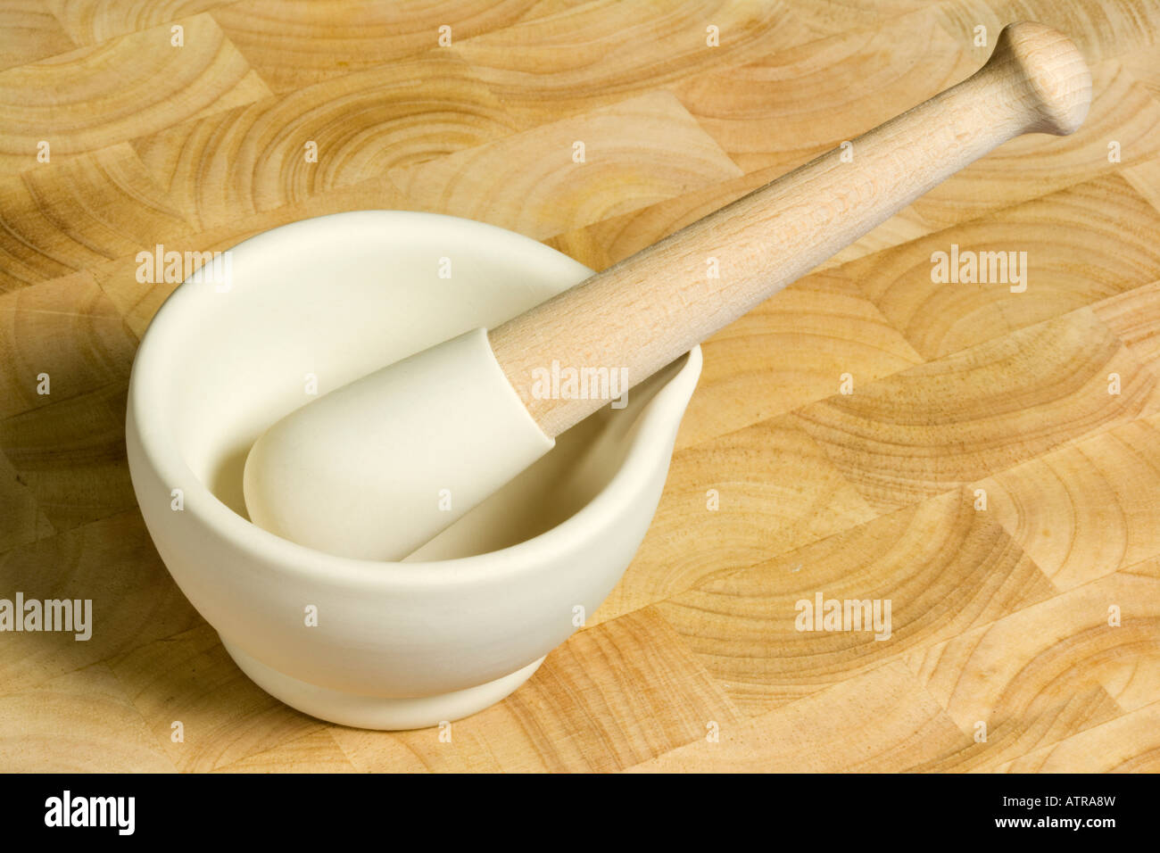 White ceramic pestle and mortar on a wooden kitchen chopping board Stock Photo