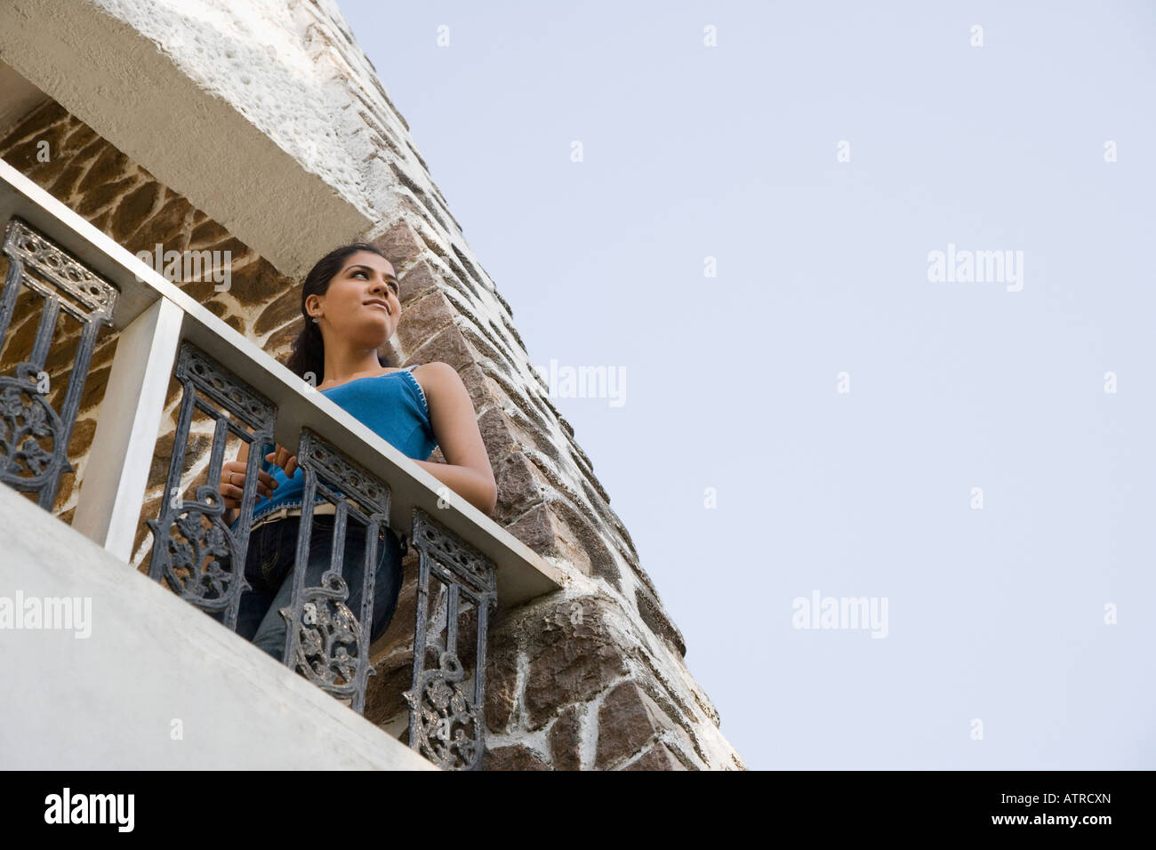 Low angle view of a young woman standing on the railing of a house ...