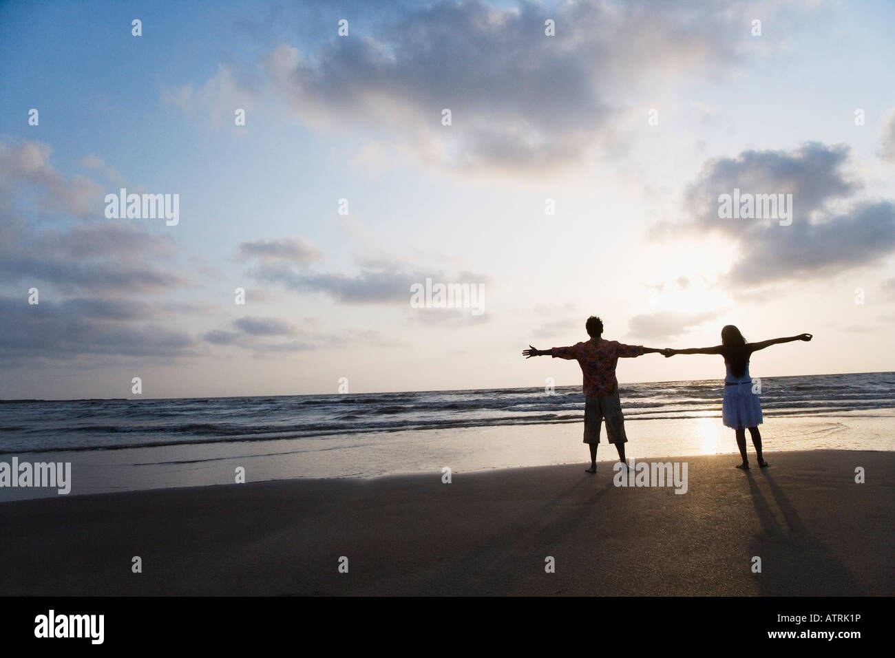 Silhouette of a young couple standing on the beach with their arms ...