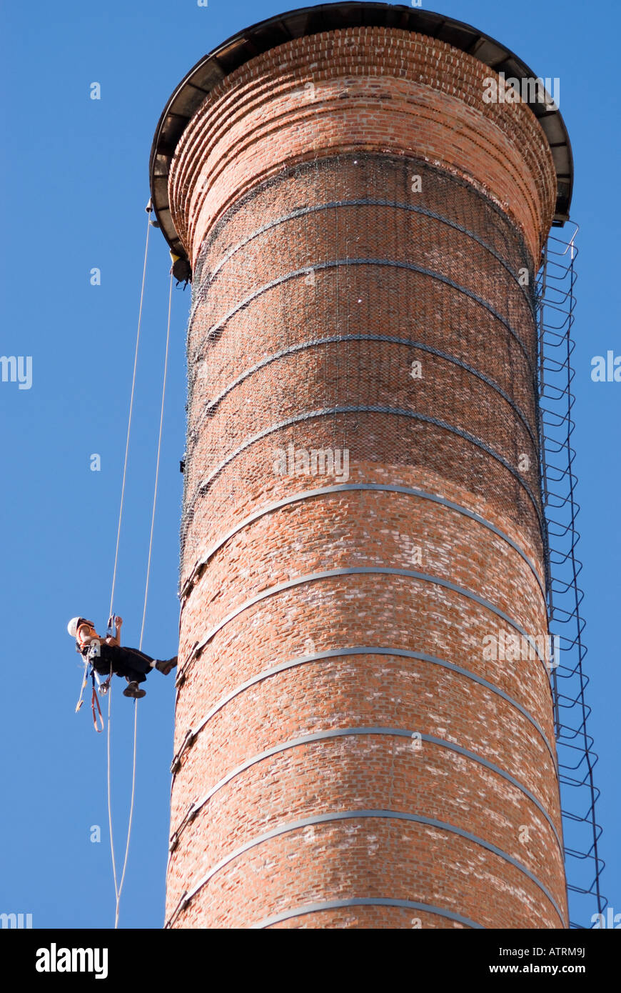 Cropped shot of an unrecognizable worker hanging from a high industrial brick chimney, running to the top. Stock Photo