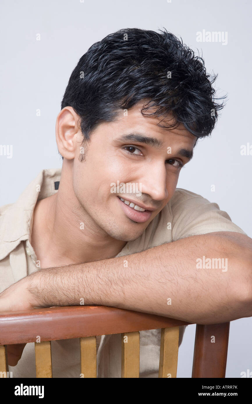Portrait of a young man sitting on a chair and smiling Stock Photo - Alamy
