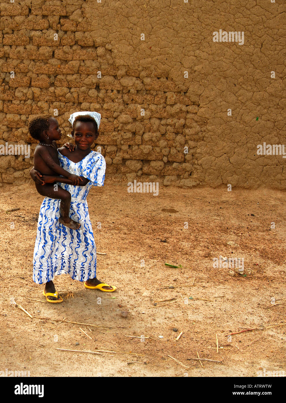 Young African girl carries her sister on the arm village scene Burkina Faso Stock Photo