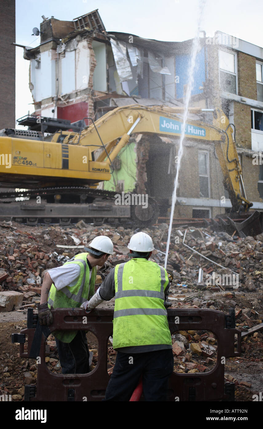 Construction workers dampen down dust with a water hose during the demolition of a housing estate. Stock Photo