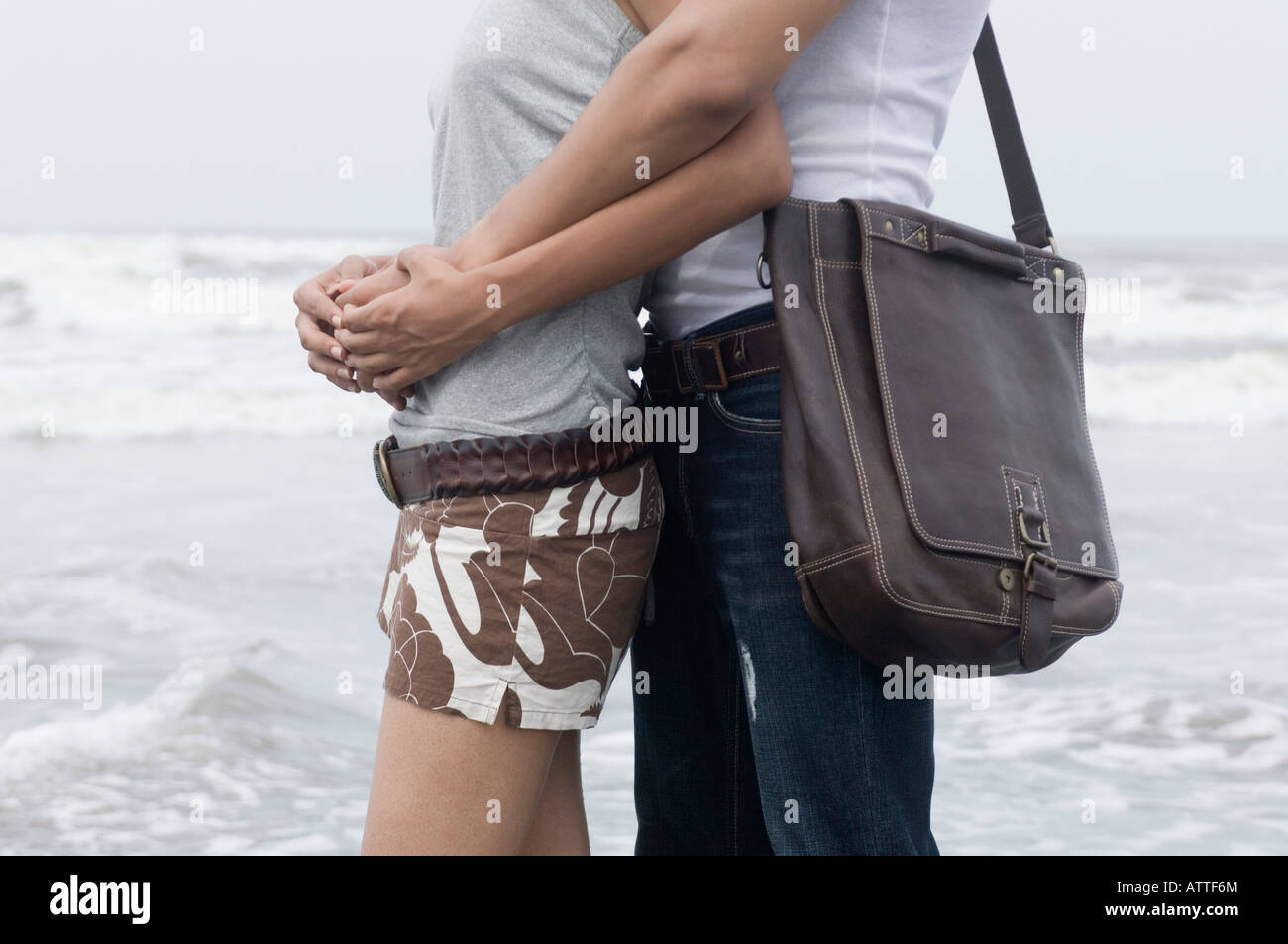 Mid section view of a man embracing a woman from behind on the beach ...
