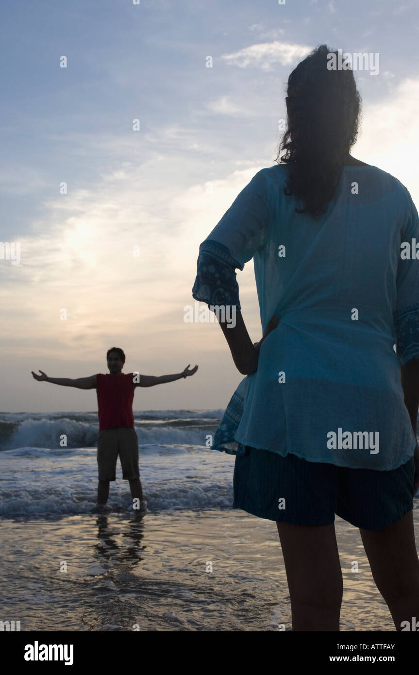 Rear view of a young woman standing on the beach with a young man ...