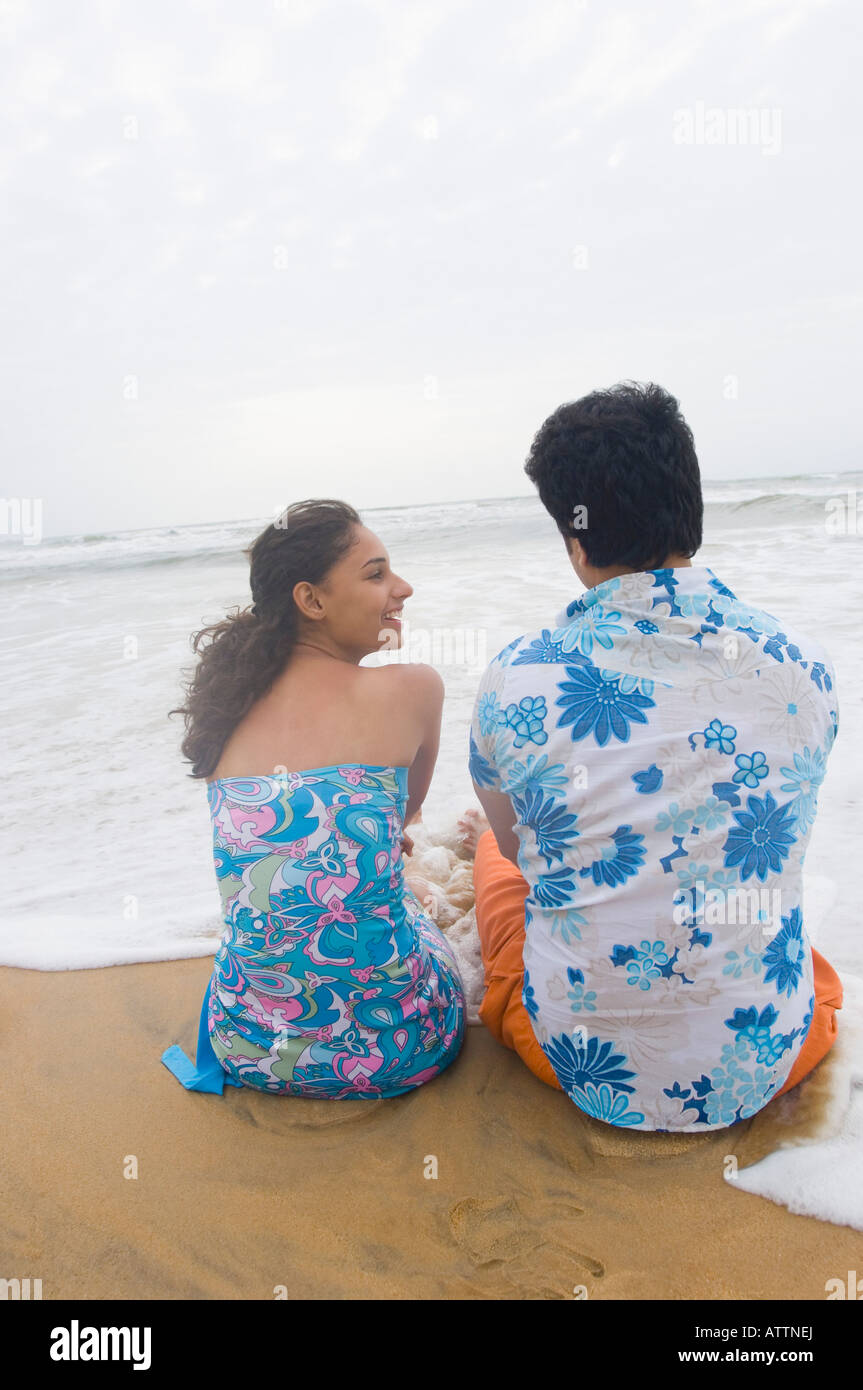 Rear view of a young couple sitting on the beach Stock Photo - Alamy