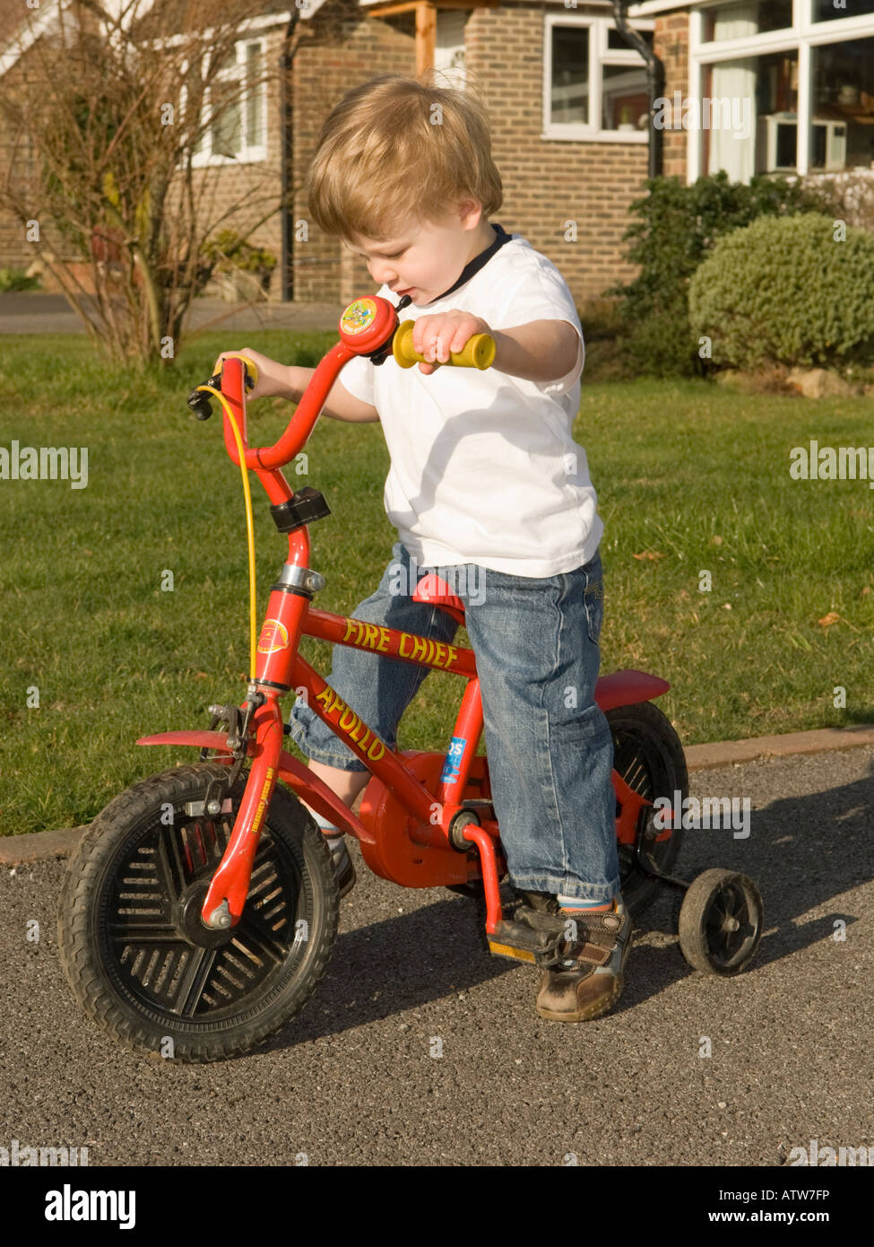two year old boy learning to ride a bike fitted with stabilisers Stock Photo