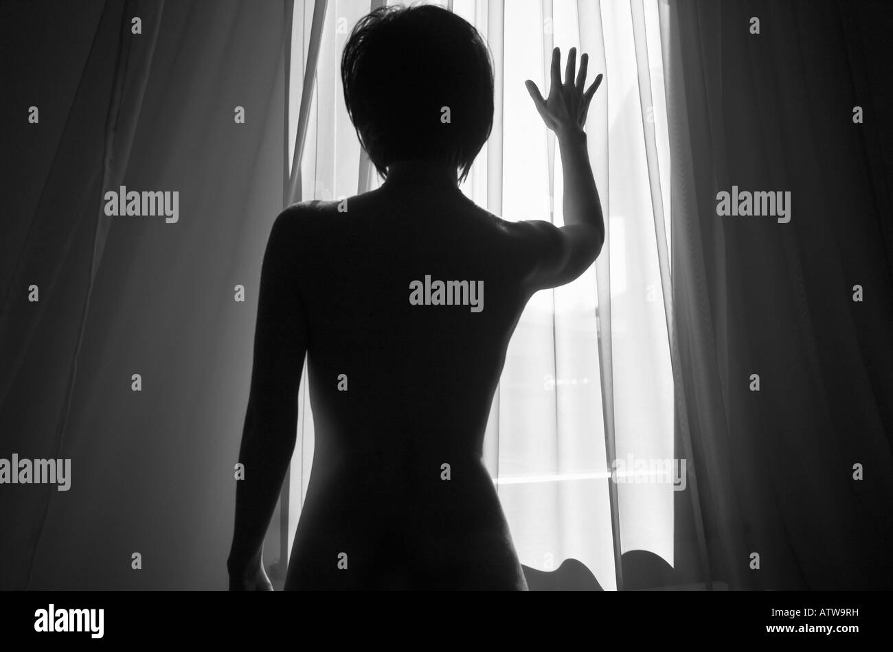 Woman silhouetted against window light placing hand on window Stock Photo