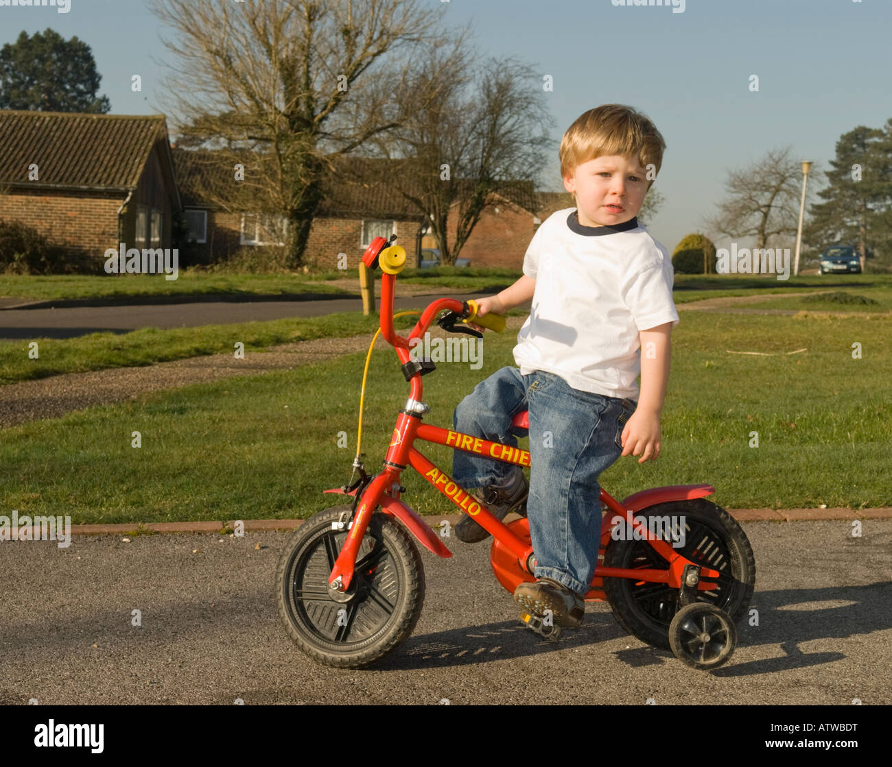 two year old boy learning to ride a bike fitted with stabilisers Stock Photo