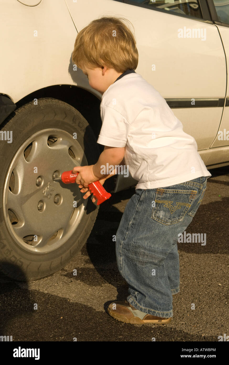 two year old boy with toy drill playing at being a mechanic working on a car Stock Photo