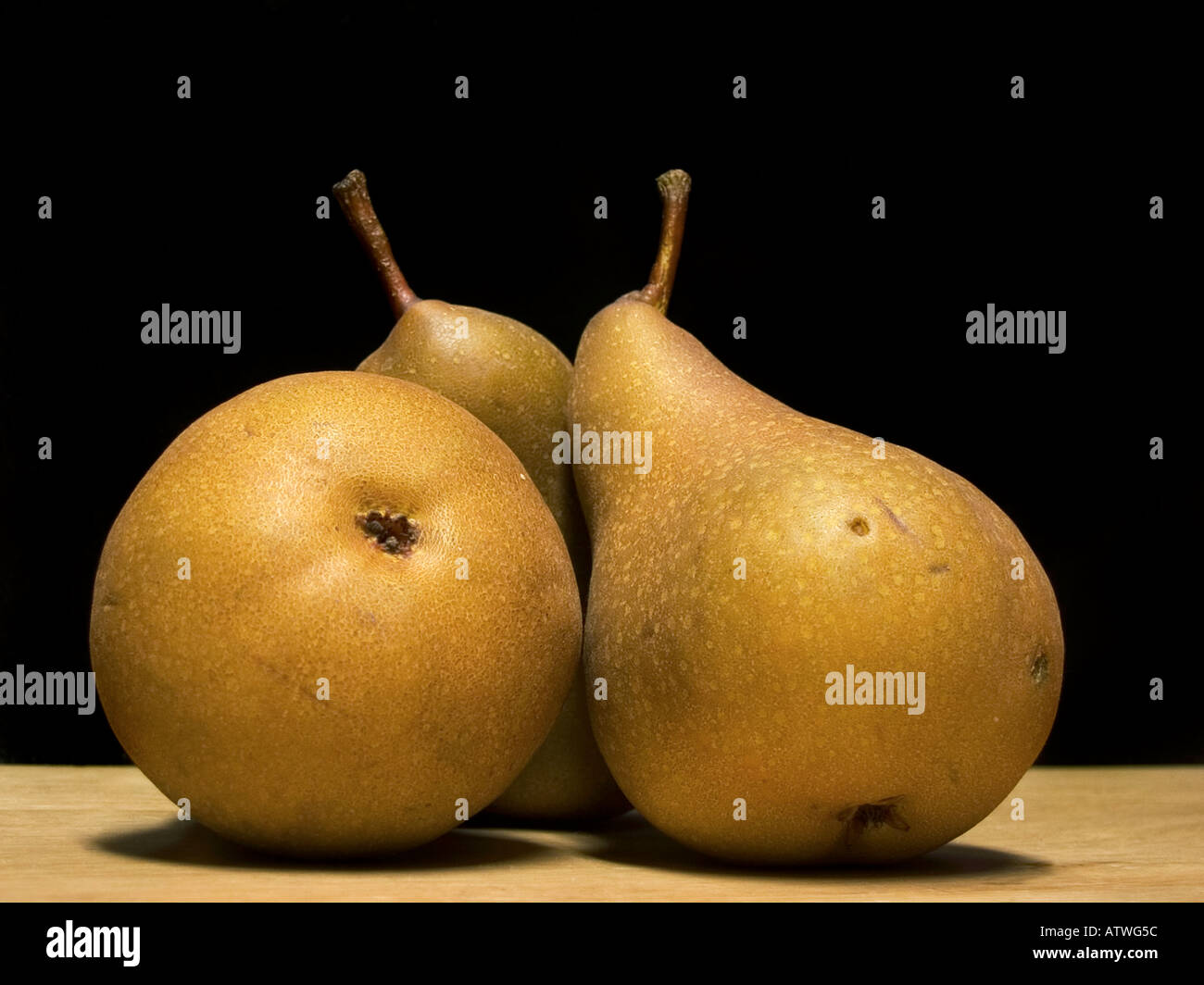 Still life image showing 3 bosc pears in warm light on a wooden table with a dark black background. Stock Photo