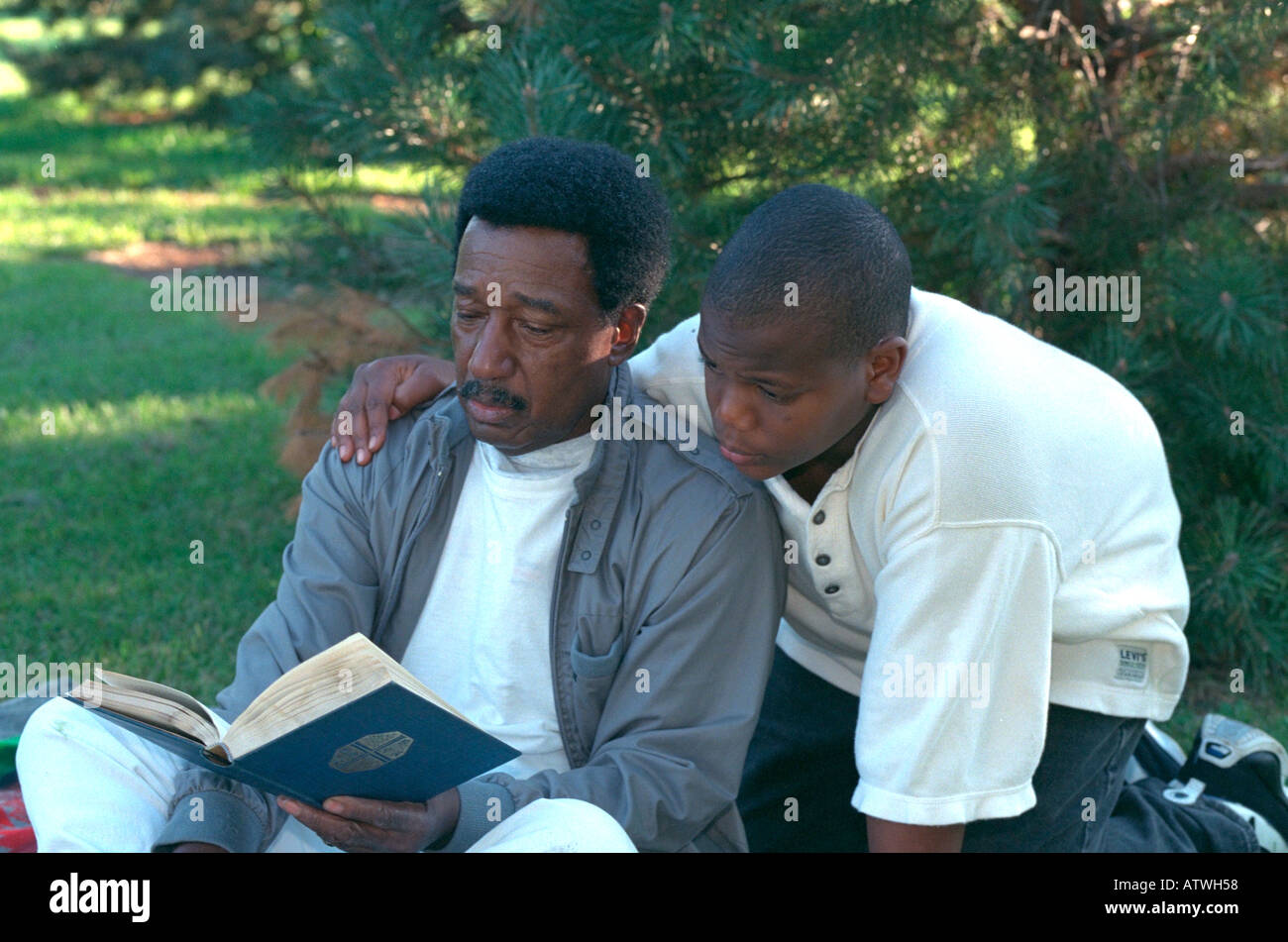 Black grandfather age 70 and grandson age 13 reading Bible in park. St Paul Minnesota USA Stock Photo