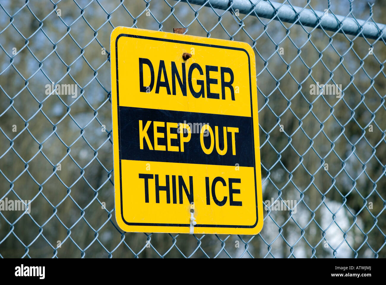 Sign reading Danger Keep Out Thin Ice hanging on a chain link fence Stock Photo
