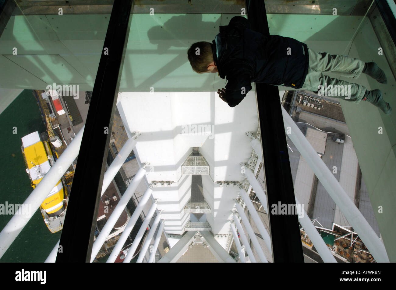 a small boy child youngster laying lying down looking through the glass walk floor in at the spinnaker tower tourists attraction Stock Photo