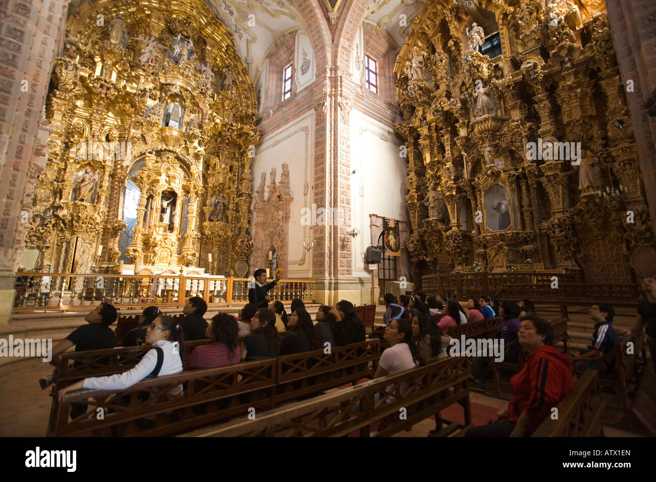 MEXICO Valenciana Gilded retablos around altar tour group listening ...