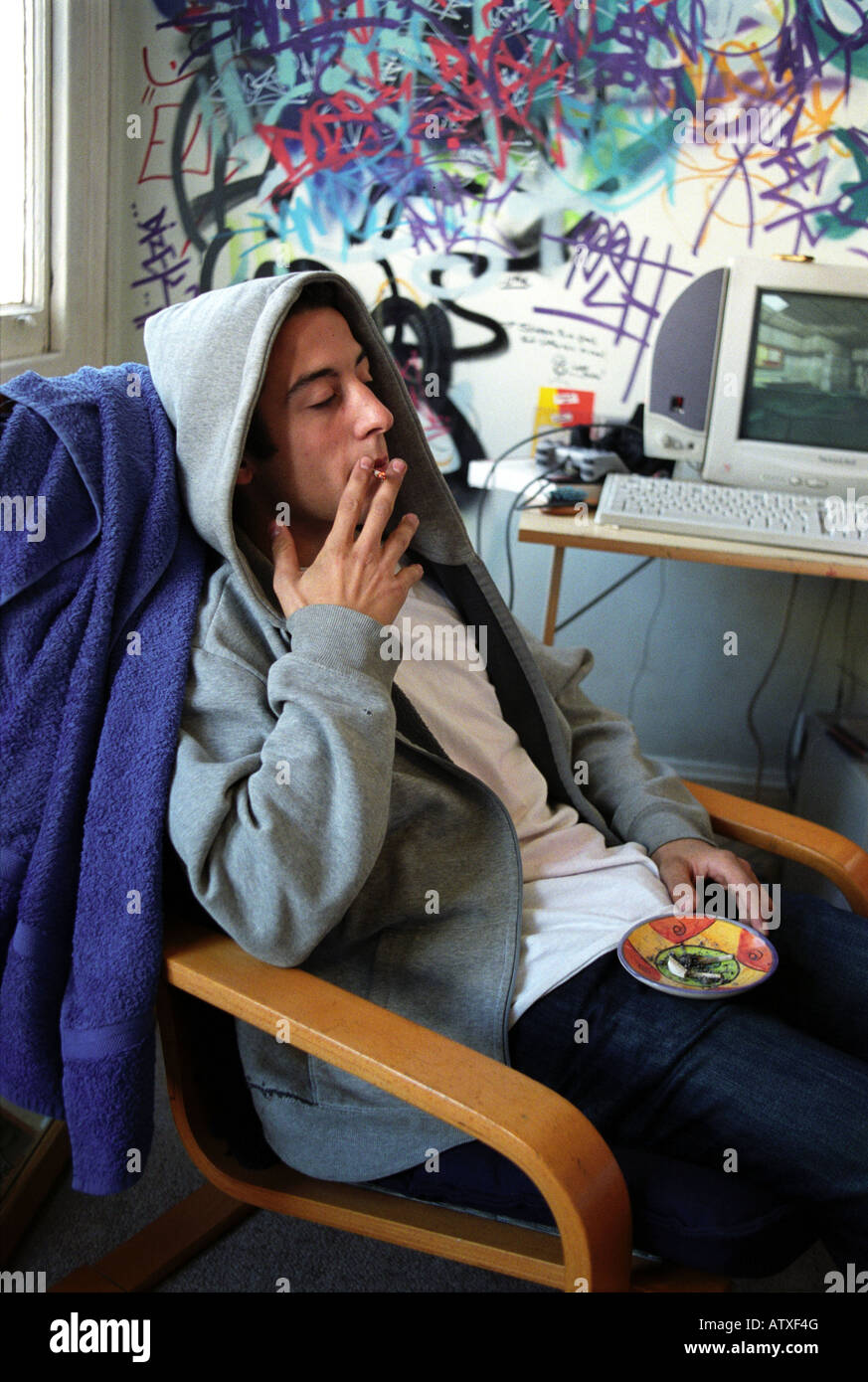 Teenager wearing a hoody and smoking a spliff  in his room. Stock Photo