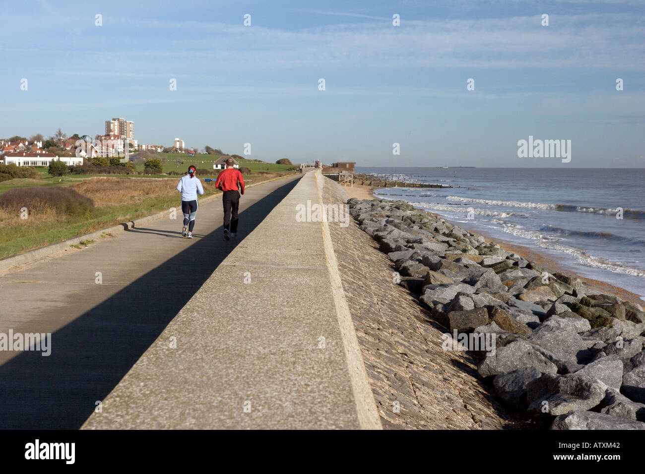Two joggers run along the seafront at Frinton on sea Stock Photo Alamy