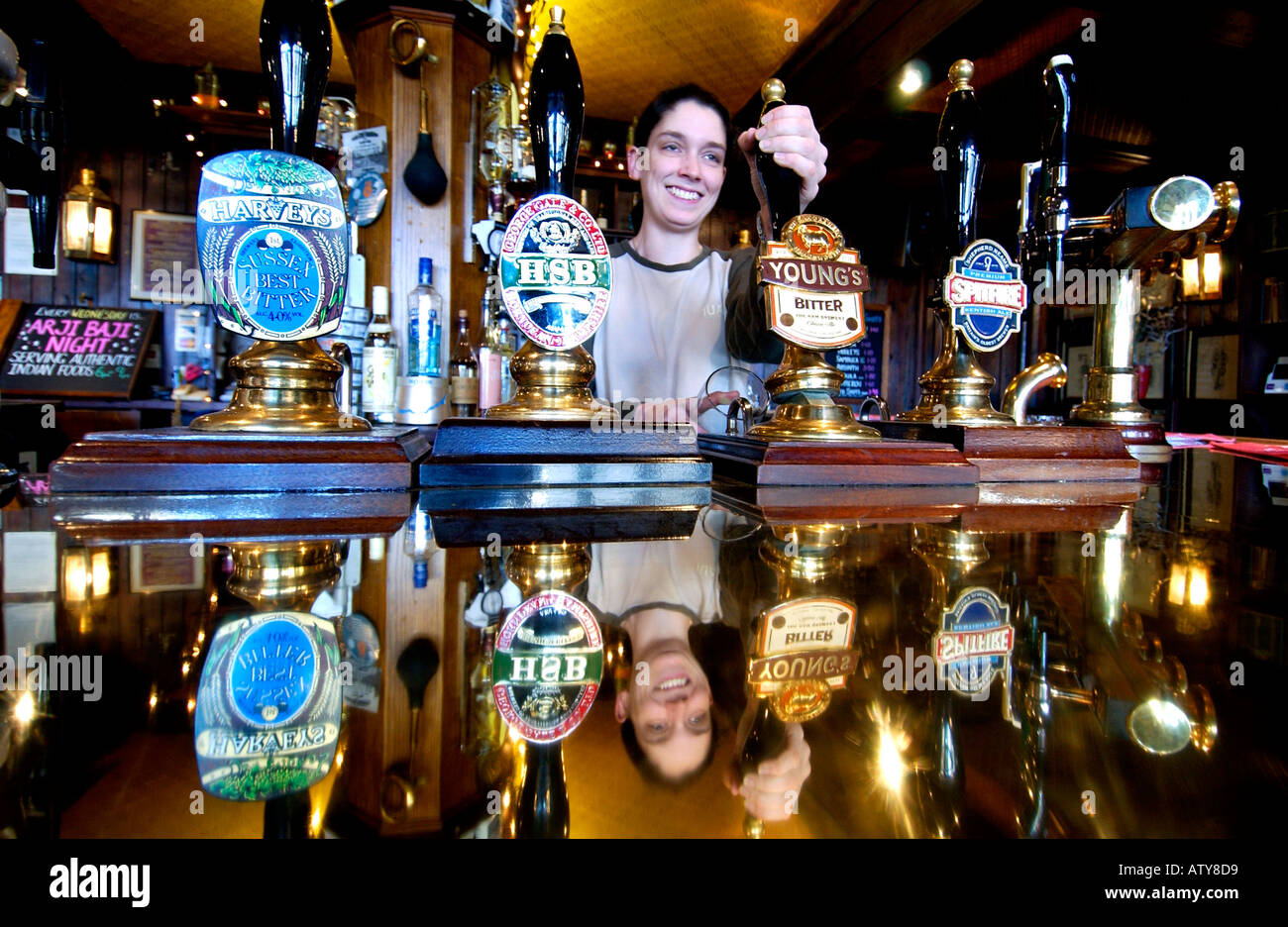 A barmaid pulls an old fashioned pint in a Victorian pub with a copper bar and real ale from handpumps Stock Photo