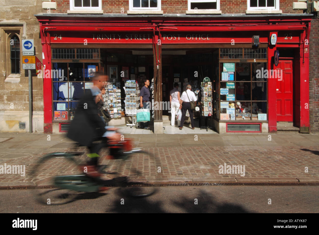 Cambridge university town Trinity Street Post Office store cyclist hurtles past Stock Photo