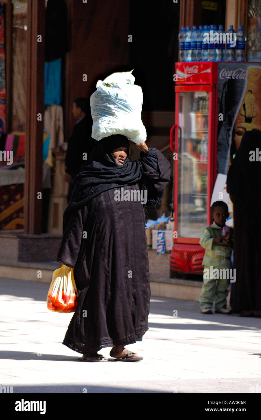 Egyptian Lady in traditional dress (maybe Nubian) carrying goods on her head in Aswan's famous souq, Aswan, Egypt Stock Photo