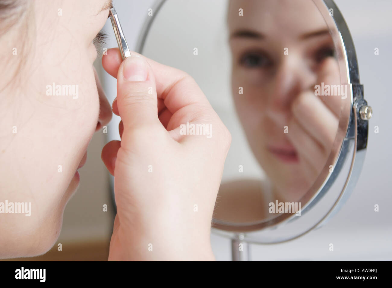 young woman plucking her eyebrows in the mirror Stock Photo Alamy